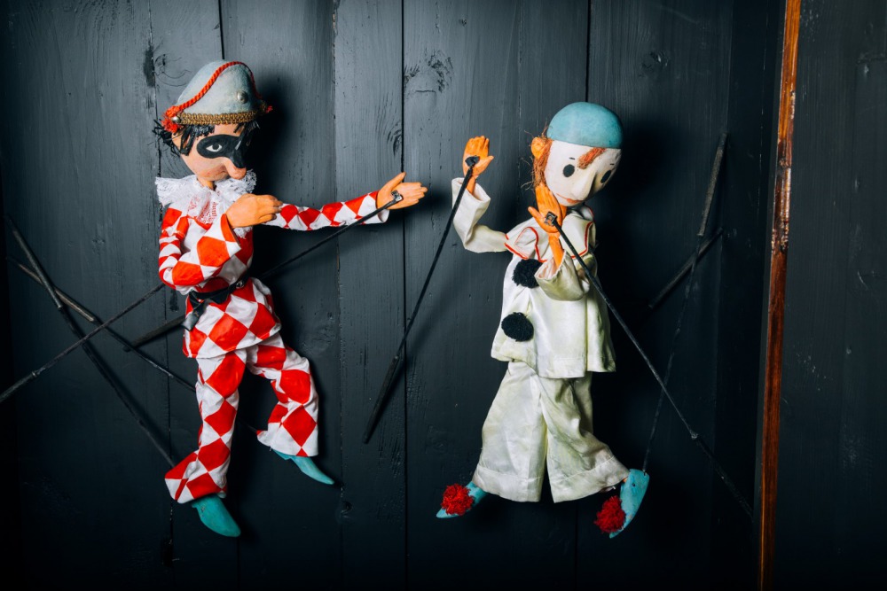 dve bábky hrajúce detskú divadelnú hru s dreveným pozadím